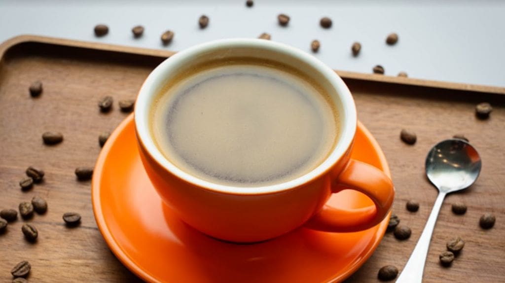 cup of brewed coffee in orange coffee mug with coffee beans