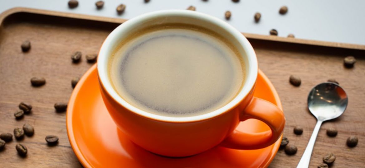 cup of brewed coffee in orange coffee mug with coffee beans